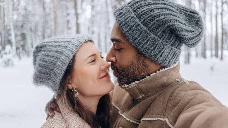 romantic young diverse couple hugging in snowy forest on winter day