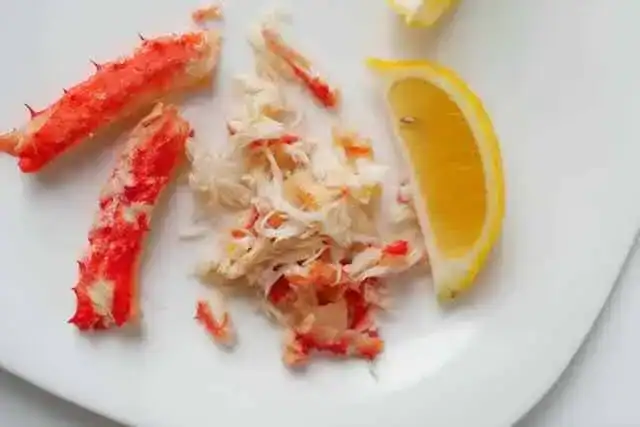 Fresh crab meat with lemon wedge on white plate.