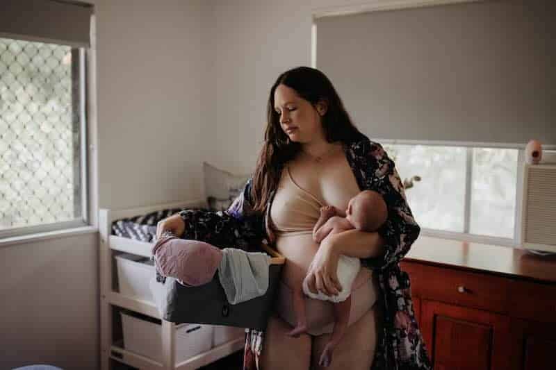 Alt text: Woman breastfeeding her baby near window in a cozy room, maternal care and bonding.