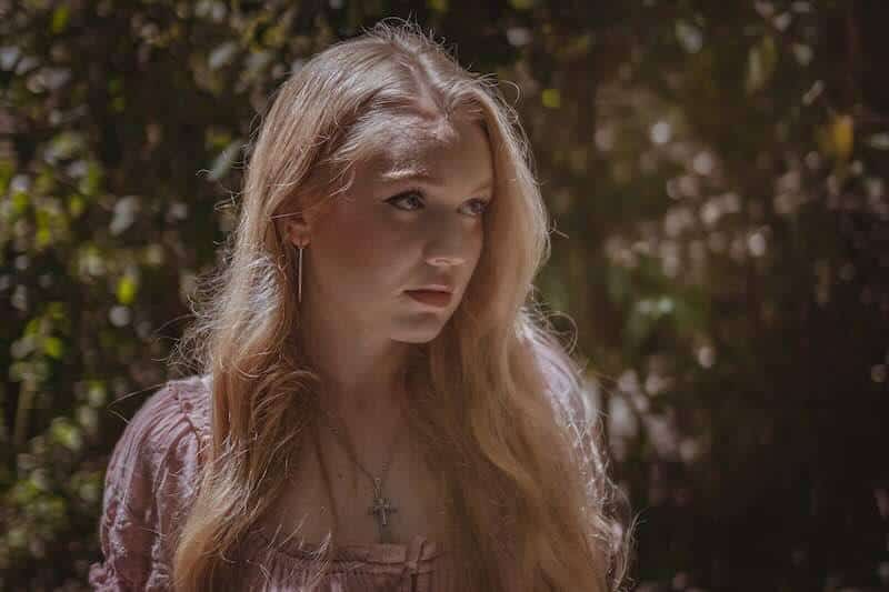 Young woman with long blonde hair in nature, soft sunlight, peaceful expression, beauty and tranquility.