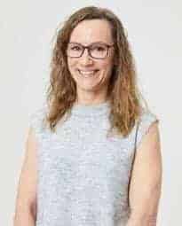 Smiling woman with glasses, casual clothing, bright background, representing confidence and positivity.