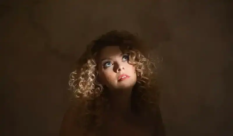 Beautiful woman with curly hair, dreamy expression, and bright blue eyes.