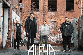 ALEYA band members standing outdoors in an urban alley with brick walls.