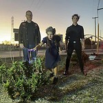 Alternative scene with three individuals outdoors at sunset, featuring a cannabis plant in the foreg.