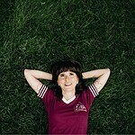 Ellie Heath lying on grass with arms behind head, smiling.