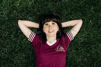 Ellie Heath lying on grass with arms behind head, smiling.