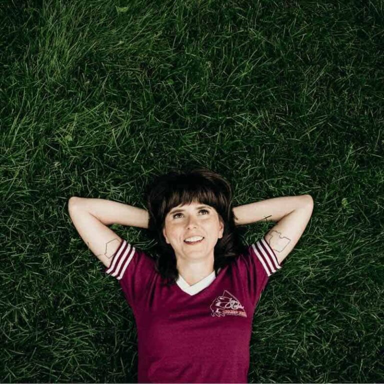 Ellie Heath lying on grass with arms behind head, smiling.