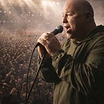 Mick Rochford singing into a microphone during a concert with a large audience.