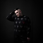 Portrait of Andrew Spice wearing a heart-patterned sweater against a dark background.