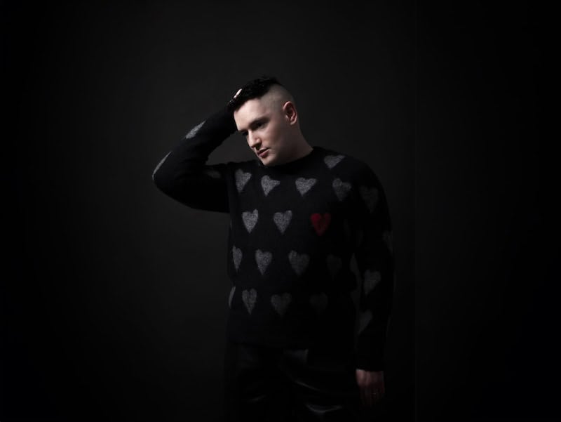 Portrait of Andrew Spice wearing a heart-patterned sweater against a dark background.