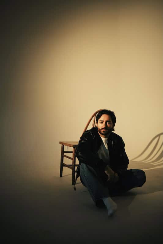 Ike Dweck seated on a chair with a neutral background, promoting his new single and US tour 2026.