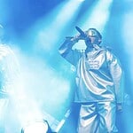 vaeb VÆB and GamerBoi performing on stage with futuristic outfits and microphones.