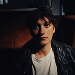 Portrait of YONAH, indie-rock artist, in a dark setting with leather jacket.