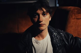 Portrait of YONAH, indie-rock artist, in a dark setting with leather jacket.